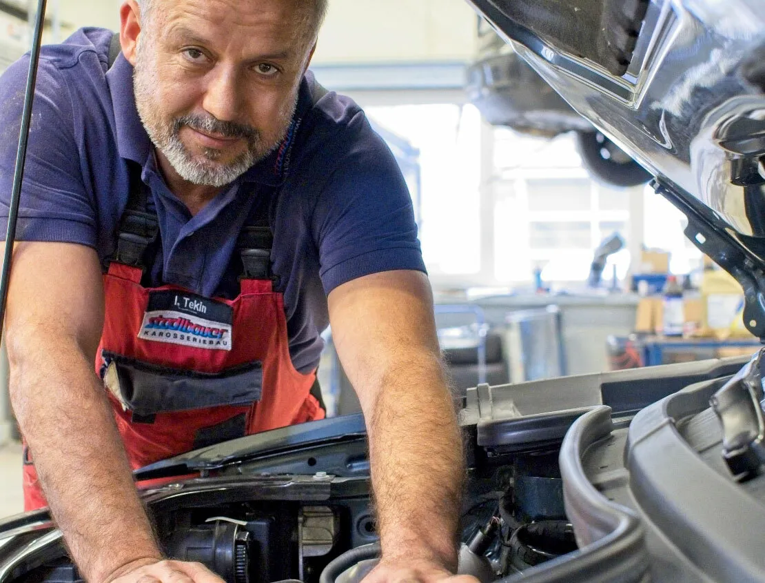Ein Werstattmechaniker schaut Sie durch die geöffnete Motorhaube an.